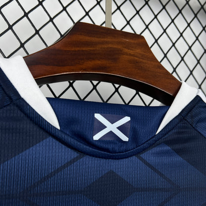 Adidas Scotland 2026 World Cup Home Blue sports jersey with a white logo on a wooden hanger against a geometric patterned wall.