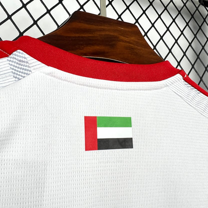 Adidas UAE 2026 World Cup Home White Jersey red collar and UAE flag patch on a hanger against a chain-link fence background.