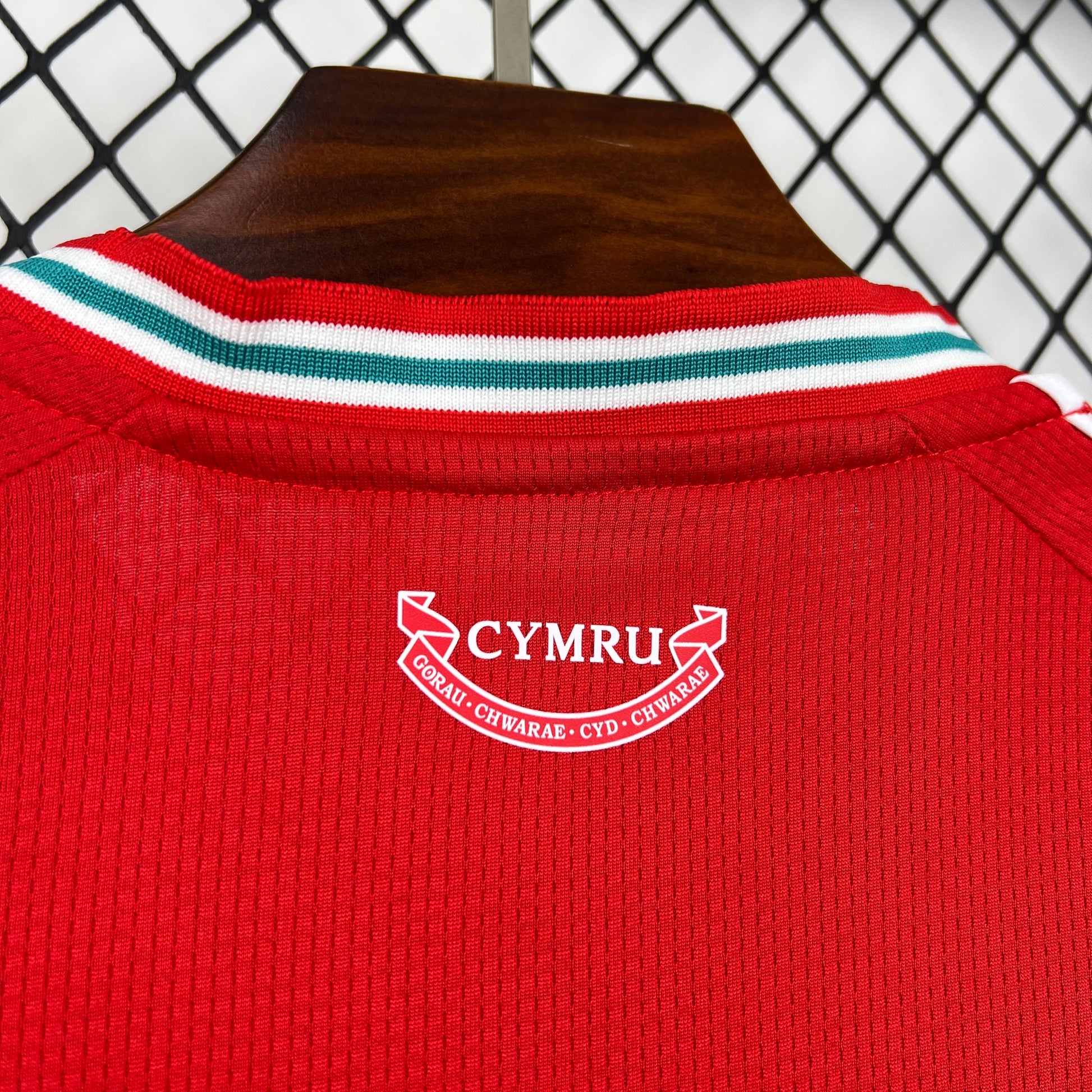 Adidas Wales 2026 World Cup Home Jersey with 'Cymru' logo on a hanger against a checkered background