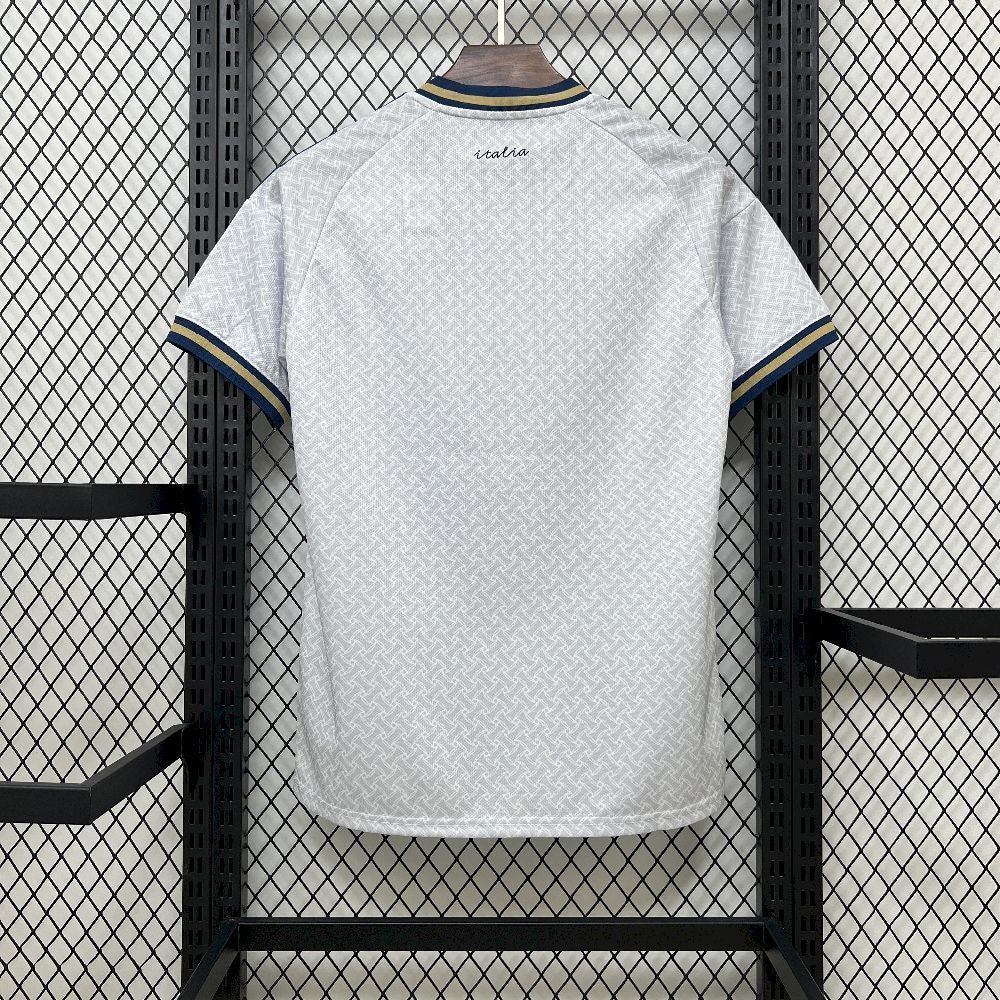 Italy 2026 Away World Cup White Jersey with blue trim hanging on a rack against a grid-patterned wall.