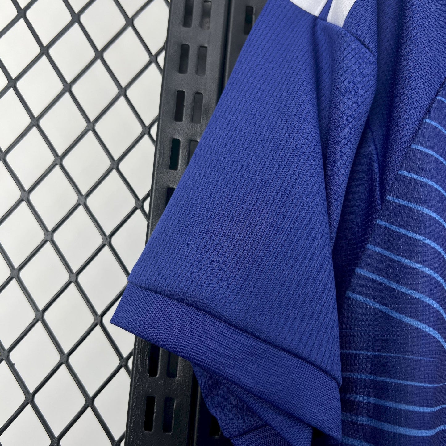Japan 2026 Home Blue Jersey - Close-up of a blue sports jersey with white stripes on a black metal rack.